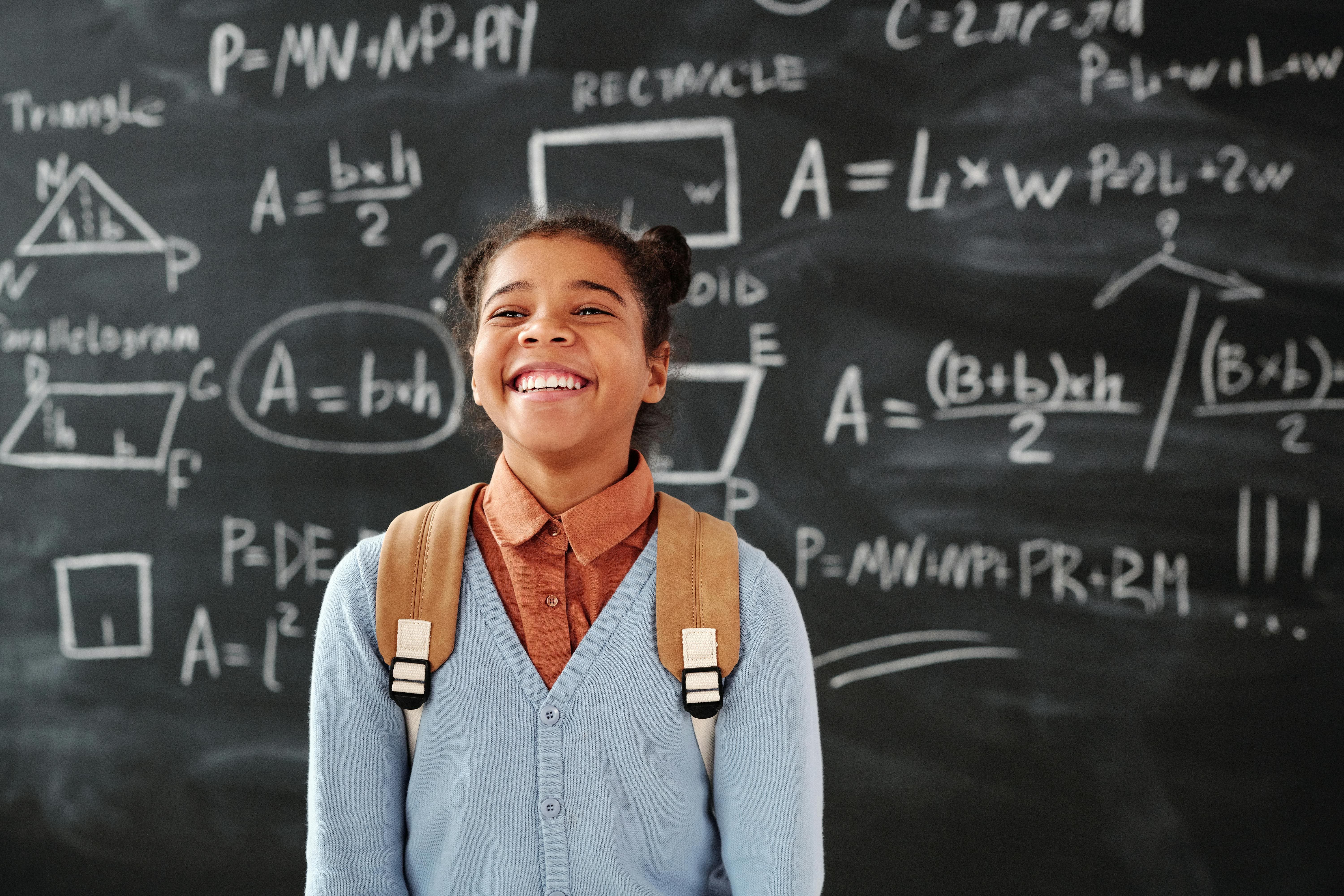 A student smiling while the backboard behind has math's formulas on it